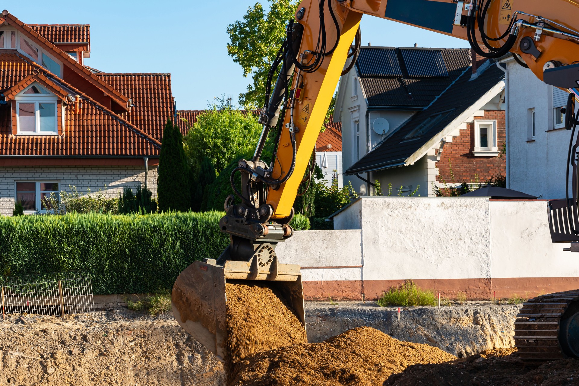 Excavator digging soil near residential area during sunny afternoon
