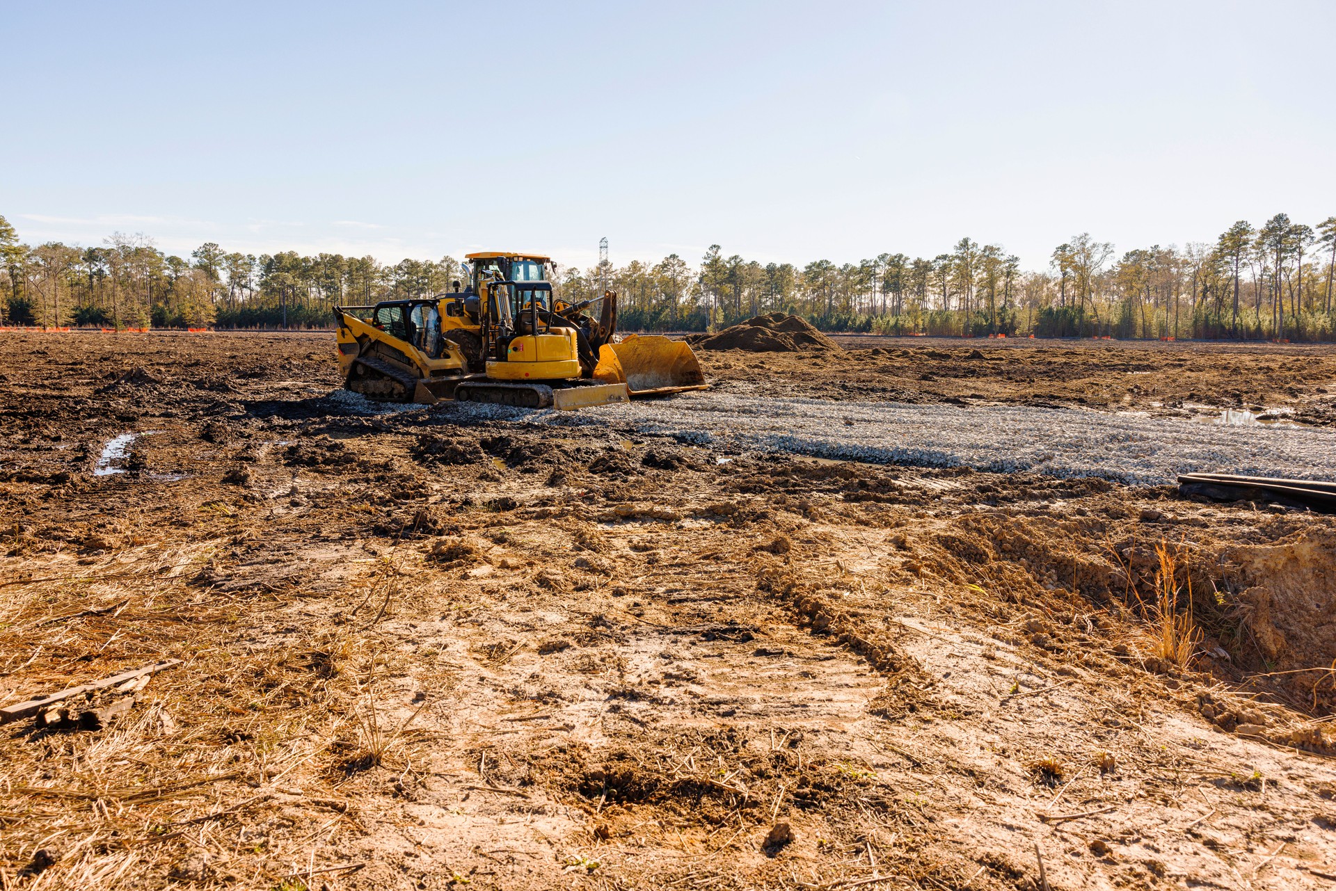 Yard for construction preparation. A yellow bulldozer is leveling the wet and dirty ground against tree area
